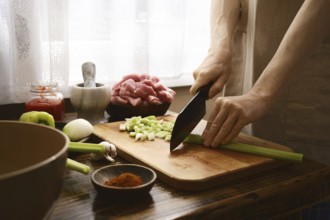 A cook prepares ingredients by chopping celery on a wooden cutting board. Fresh vegetables and