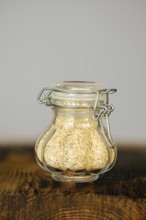 Glass jar filled with garlic flakes on a wooden surface against a neutral background