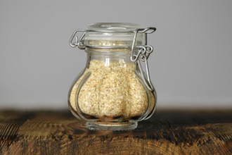 A small, decorative glass jar with garlic flakes, showcasing its fine texture and color on a rustic