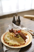 A hearty serving of creamy mashed potatoes topped with tender meat and vegetables on a rustic