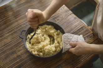 Hands mashing cooked potatoes in a pot. The process highlights a home-cooked meal preparation