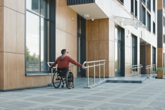 A person in a red hoodie navigates a wheelchair along a smooth ramp outside a contemporary
