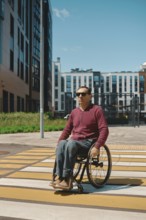 A man in a wheelchair navigates a crosswalk marked with yellow lines in a contemporary city