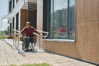 Individual in a wheelchair is utilizing a ramp to exit a modern building with large windows. The