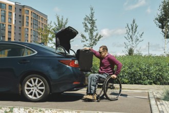 A person in a wheelchair is carefully placing a suitcase into the trunk of a parked car. The
