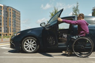 A man in a wheelchair approaches a car parked in a bright urban setting. He is wearing a purple