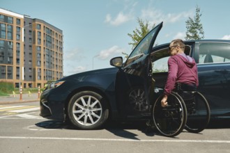 A man in a wheelchair is using his arms to propel himself into a parked vehicle with an open door.