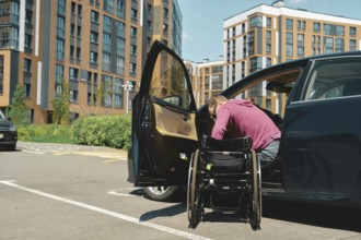 A man moves to a wheelchair from a car parked at a lot for people with disabilities in a