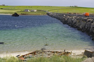 Ruin of a boat on the beach with a breakwater and green coastal background, Churchill Bariers,