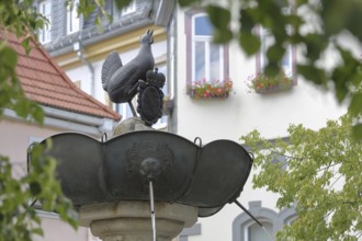 Hennebrunnen fountain with sculpture and coat of arms with crown, bird figure, market square, town
