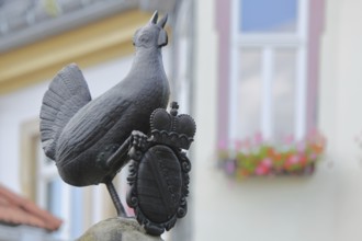 Grey bronze sculpture and coat of arms with crown at the Hennebrunnen fountain, bird figure,