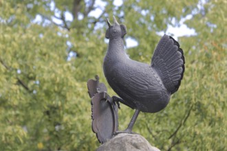 Grey bronze sculpture at the Hennebrunnen fountain, bird figure, screaming, tail feathers, market