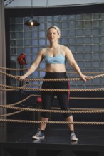 A focused female boxer stands confidently within a boxing ring constructed with ropes, wearing