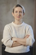 A woman poses confidently with her arms crossed, dressed in a soft, knitted sweater