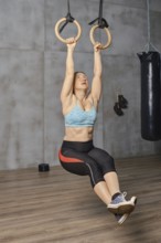A determined woman engages in a core-strengthening workout while hanging from gymnastic rings