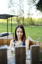 A woman enjoys a serene moment in a wooden hot tub, immersed in warm water, while surrounded by