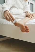 Close-up view of peeling dead skin off heel with handheld electric exfoliating machine in bedroom