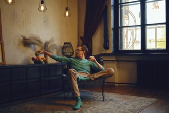 A man sits comfortably in a contemporary chair, casually extending his arm to grab fruit from a