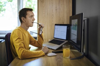 A man in a yellow shirt sits at a desk in his home office, studying data on his computer and bites