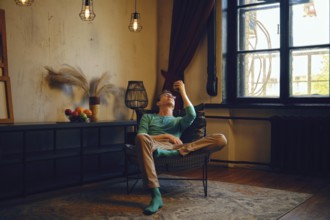 A man sits comfortably in a chair, gazing thoughtfully at an apple in his hand. Soft lighting and