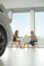 A customer and a salesperson are engaged in a discussion at a small table inside a sleek car