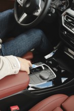 A person in casual attire sits in the driver's seat of a modern vehicle, reaching to adjust the