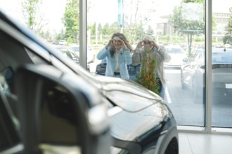 Couple put their hands on the glass peering through large windows at car showroom