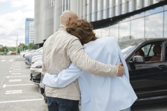 A couple stands affectionately close while considering car options at an automobile dealership.