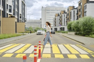 A woman with long hair walks across a marked pedestrian crossing in a contemporary urban area. She