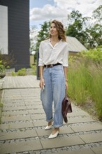 A young woman is walking along a stone path, wearing a white shirt and light blue baggy jeans. She