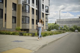 A woman strolls down a sidewalk in a vibrant urban area. She wears a stylish outfit and walks past
