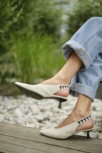 A woman showcases fashionable white slingback heels while sitting outdoors. She wears rolled-up