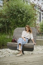 A woman sits comfortably on a contemporary bench in a landscaped area filled with lush green plants