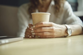 A person enjoys a peaceful moment in a cozy cafe, holding a paper cup of coffee. Hands rest