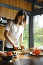 Woman chopping ginger in a bright kitchen with fresh vegetables on a wooden table