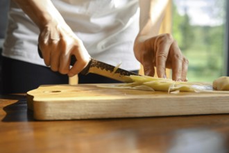 Unrecognizable person skillfully slices fresh ginger on a wooden cutting board in a well-lit
