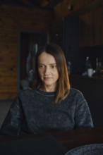 A woman with medium-length brown hair sits at a dark wooden table, reflecting thoughtfully. The