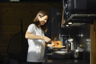 A woman takes out fried vegetables from the pan with kitchen tongs standing by the stove in a