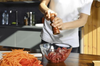 Unrecognizable person seasons fresh beef meat with pepper while preparing a healthy meal in a