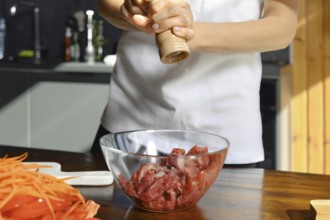 Unrecognizable person is adding freshly ground salt to a bowl of diced meat, preparing for a
