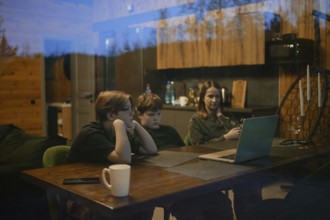 Inside a cozy cabin, a family gathers around a table enjoying a shared experience. Two children are