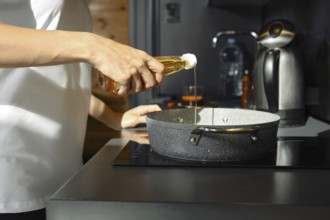 A person pours sesame oil into a saucepan while preparing a healthy meal in a modern kitchen. The