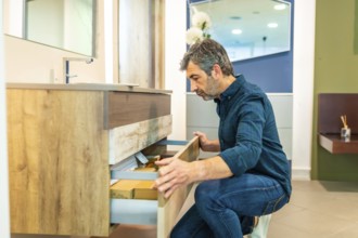 Mature man crouching, opening drawers of a bathroom vanity, checking quality and organization in a