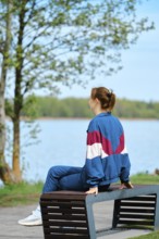 A person sits on a bench by a serene lake surrounded by lush greenery, enjoying the calm atmosphere