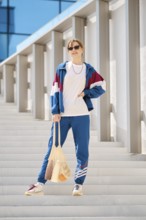A young woman stands on a series of outdoor steps, wearing a colorful sports outfit with sunglasses