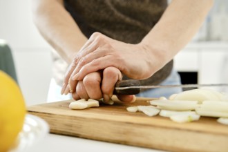 Unrecognizable woman crush garlic to finely chop it for sauce on a wooden cutting board in a bright