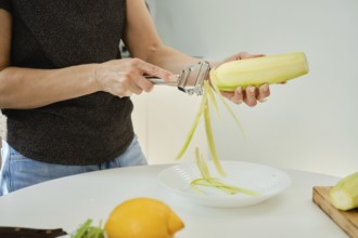 Unrecognizable woman skillfully cuts zucchini into strips with a hand-held tool and cooks vegetable