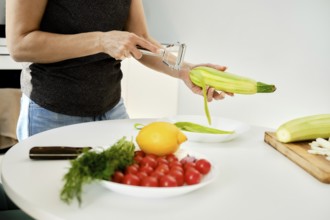 A person prepares fresh vegetables in a modern kitchen, peeling zucchini while other ingredients,