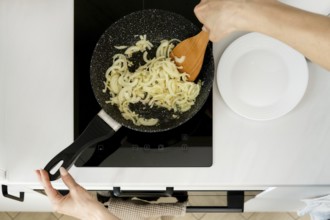 Cooking onions in a skillet on a modern kitchen stovetop with a wooden spoon
