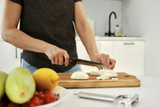 A person is slicing fresh onion on a wooden cutting board in a sleek kitchen. Colorful fruits and